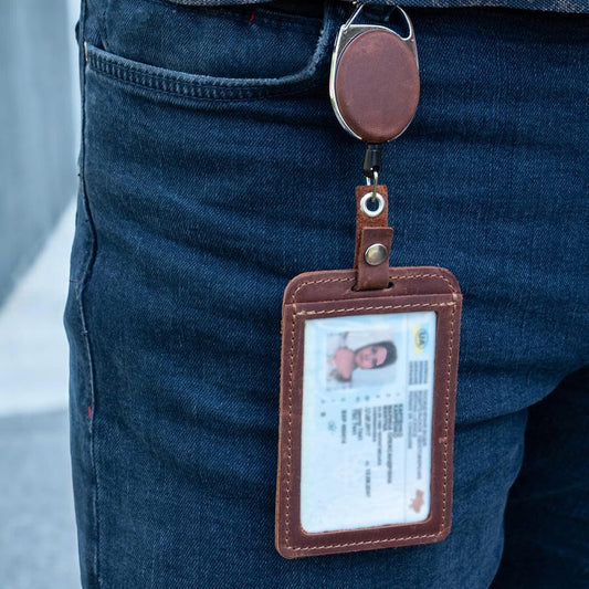 Brown leather ID card holder with retractable reel and metal clip, showing transparent ID window